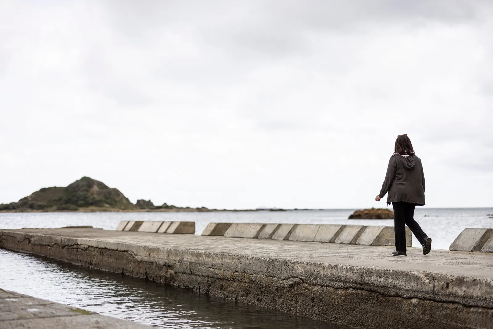 A woman walking along a sea wall on the Wellington coast